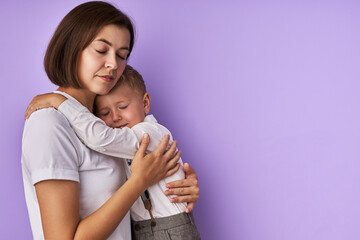 sleepy caucasian child boy with mother isolated over purple background, woman hugs her son, they stand with closed eyes, want to sleep