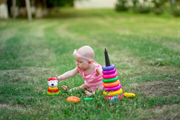 baby girl 10 months old sitting on the grass in the summer and playing pyramid, early development of children, outdoor games