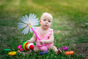 baby girl 10 months old sitting on the grass in the summer and playing with a turntable, early development of children, outdoor games