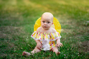 baby girl 10 months old sitting on the grass in summer in a yellow dress, walking in the fresh air