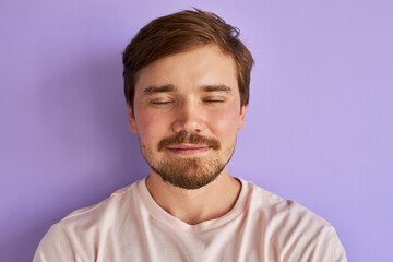 man keeps calm with eyes closed, isolated over purple background. handsome bearded male think about...