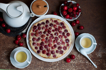 Tart with ripe sweet cherries and green tea on brown background. Homemade dessert with ripe sweet cherries. Top view