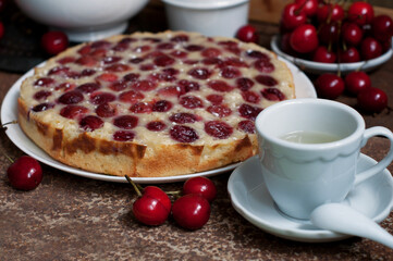 Tart with ripe sweet cherries and green tea on brown background. Homemade dessert with ripe sweet cherries