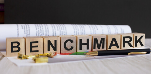 The word BENCHMARK is written on wooden cubes near the document and pen. Business concept