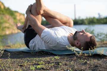 Naklejka na ściany i meble Young man doing yoga in morning park. Bearded man relax and streching in nature. International Day of Yoga