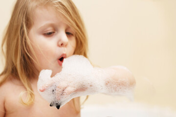 Funny little baby girl with blond hair playing with foam in a bath tub. girl takes a bath
