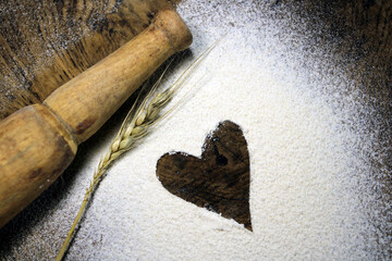 Fresh harvested wheat grain on wheat flour background. Baking concept on wood background, sprinkled flour with heart. Heart drawn in scattered flour alongside a wooden rolling pin on wooden background
