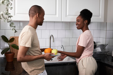 friendly afro american married couple in the kitchen, woman wash fresh fruits, man helps her, stand next to her and talk