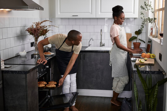 young married african couple is cooking, baking together. they are happy that everything turns out, use oven