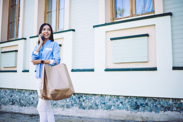 Happy female shopaholic feeling excited after shopping during Black Friday and calling to friend for tell news about sales in mall using roaming connection for communicate via cellular phone