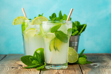 Two homemade lemonade or mojito cocktail with lime, mint and ice cubes in a glass on a light stone table. Fresh summer drink.