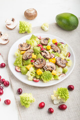 Vegetarian salad from romanesco cabbage, champignons, cranberry, avocado and pumpkin on a white wooden background. side view.