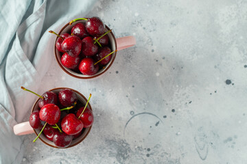 Two pink mugs with fresh ripe cherries. Sweet organic berries on a light concrete background. Top view with copy space