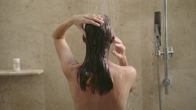 Young slender woman washes hair in the shower