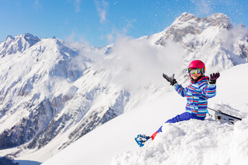 Fototapeta na wymiar Happy girl sit in snow on top of the mountain and lift hand in ski outfit, color mask, pink helmet