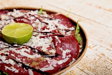 Plate of delicious Mexican Carpaccio dish with lime on a wooden table
