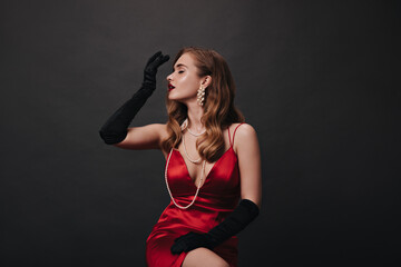 Charming lady woman in red silk dress posing on isolated background. Attractive lady in satin outfit sitting on black backdrop