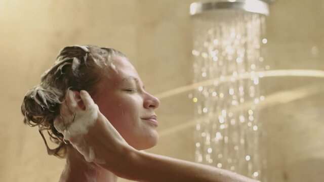 Young slender woman washes hair in the shower. Slow motion.