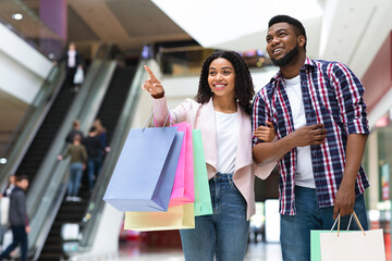 Shopping Together. Black Woman Pointing At Something In Mall, Showing To Boyfriend