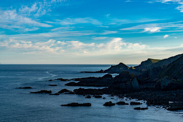 Sea shore with sharp rocks and cliffs during sunrise under blue sky with intermittent clouds