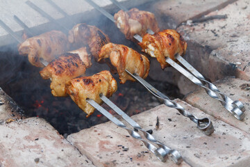 Close-up of chicken legs strung on skewers and fried over an open fire, selective focus
