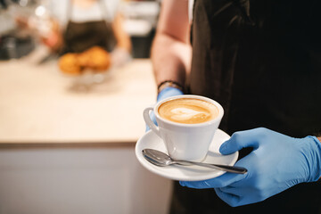 Unrecognizable waitress with gloves working in cafe, holding cup of coffee.
