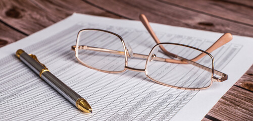 On a dark wooden table lies a document with a pen and glasses in a golden frame. Top view close up. Business concept