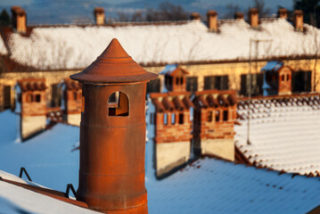 Top view of chimneys and roofs of snowy houses illuminated by the setting sun