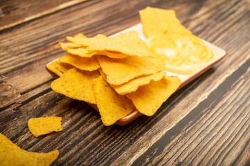 Corn chips with cheese sauce on a wooden background. Close up.