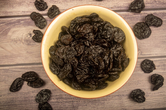 Dried prunes in a ceramic bowl and dried prunes scattered on a wooden background. Close up.