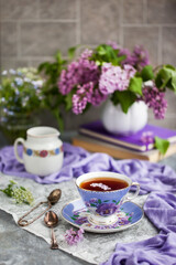 Purple cup of tea and lilac on gray background