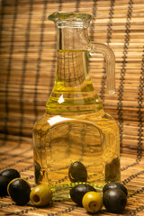 A bottle of olive oil on a background of green olives, black olives and a reed Mat. Close up.