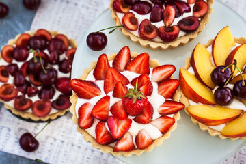 Fresh delicious cherry, strawberry and peach tartlets on gray background