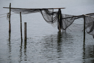 Fishing nets hanging on wooden posts in a lake on a cloudy day