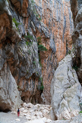 Fototapeta na wymiar A woman is walking between the red rocks of the canyon Gorropu in Urzulei, Sardinia