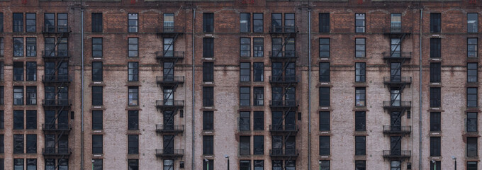 Widescreen image of a red brick classical industrial building in New York with fire escape ladders,...