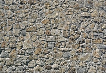Massive stone wall made of gray and brown rocks with irregular shapes. Background and texture