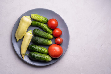 Group of freshly harvested young cucumbers, tomatoes, peppers and herbs grown in a greenhouse, lies on a wooden table. Healthy eating concept.