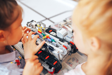 Two schoolgirls study in a robotics class, assemble a robot constructor.