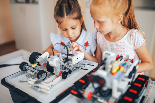 Two schoolgirls study in a robotics class, assemble a robot constructor.