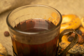 tea, driedA faceted glass of tea in a vintage Cup holder, dried rosehip fruit and small bagels on a background of homespun fabric with a rough texture. Close up. rosehip fruit