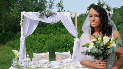 The bride with a veil in front of the wedding table holds a bouquet.