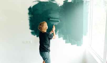 Fototapeta premium Little boy a preschooler paints in the room by the wall roller. The child helps to repair the parents.