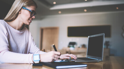 Young hipster girl freelancer using web notepad at coworking space earning money by internet website, woman communicates in social networks with people via laptop computer with mockup screen