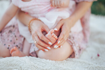 Little newborn baby in a pink dress with mom on a white plaid in a park.