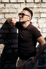 Obraz premium stylish guy with glasses stands near a stone wall and looks away. thought. strong and strict male gaze. sunlight. half-length portrait. looks up