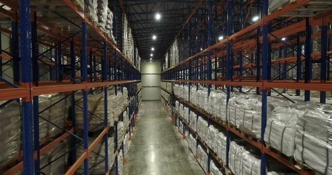 Top view, drone shot of rows of pallets in warehouse. A path through racks of goods. Camera going forward.