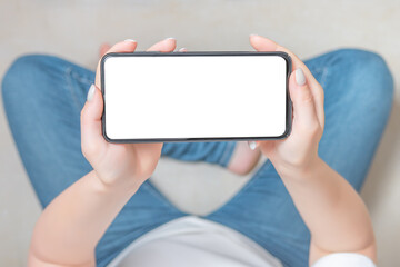Mockup image blank white screen cell phone. female hands holding texting using mobile phone on sofa at home. cell phone in horizontal position. Empty space for advertise text.