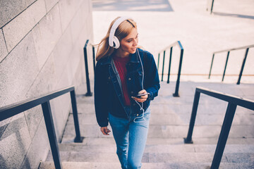 Stylish young woman in modern white headphones listening electronic music downloaded on own...