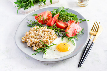 Breakfast oatmeal porridge with fried egg, tomatoes, arugula. Healthy food.